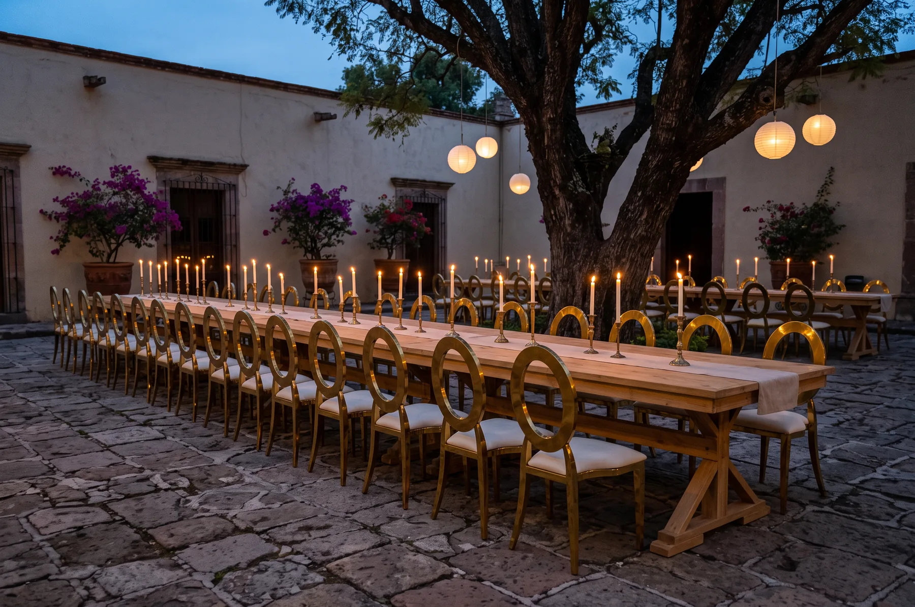 Velas altas, faroles de papel y luz escondida sobre mesa Toscana con sillas Victoria.
